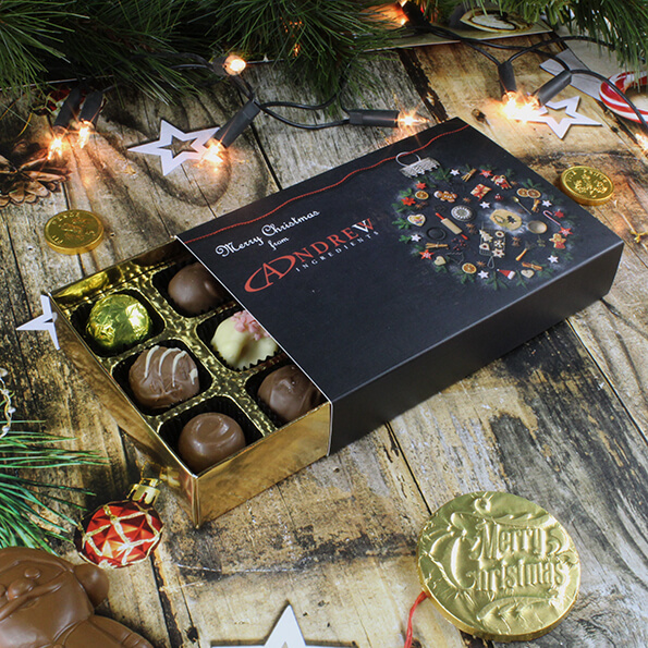 A box of handmade assorted Belgian chocolate truffles in a business branded box, sitting under a Christmas tree.
