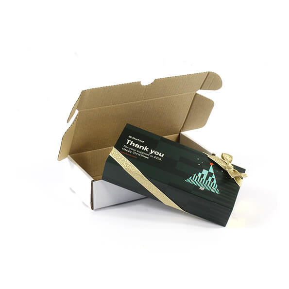 A business branded box of luxury chocolates, with a Christmas tree design print, finished with a gold ribbon and sitting on a postal outer.
