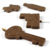 Chocolate lollipops in varied shapes, including a train, key, and rectangular bar, are arranged on a white background.