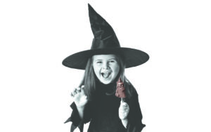 Child wearing a witch costume and holding a witch-shaped lollipop, smiling widely.
