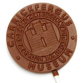 Logo Chocolate Lollipops with an embossed design resembling a historical seal, showcasing a castle and the inscription "Carrickfergus Museum.