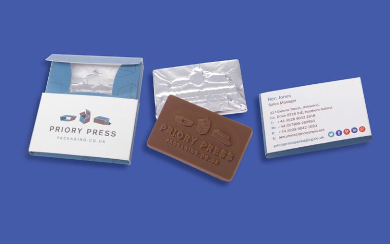 Business card and chocolate bar with Priory Press Packaging branding on a blue background.