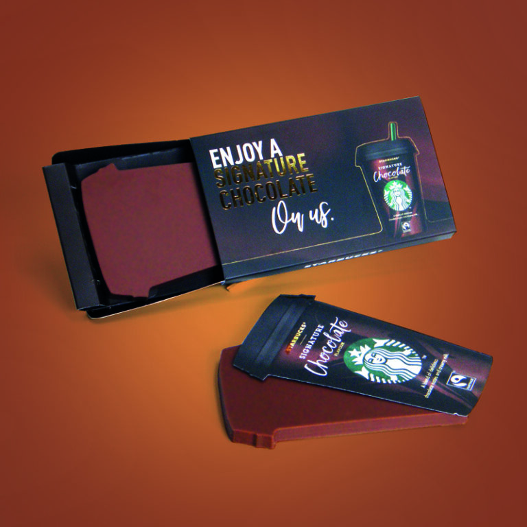 A boxed dark chocolate slab is styled to resemble a Starbucks cup, with promotional text on the packaging.