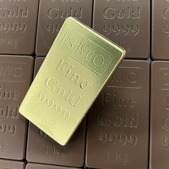 A gold bar labeled "SMIO Fine Gold 9999 1 kg" is displayed on a background of similar brown bars.