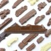 A variety of vehicle-shaped chocolates, such as the chocolate cruise ship along with cars, buses, motorcycles, and boats, are displayed on a white surface.