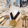 dame_mary_-_feb_24_-_2_1 Table setting with silverware, glassware, and a folded napkin adorned with a Corporate Chocolate Medal.