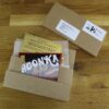 golden_ticket_bar A cardboard envelope is open on a wooden surface, exposing a golden ticket and a candy bar with the label "Chocolate Bar Fulfilment Service." A shipping label is seen partially nearby.
