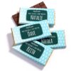 Four Personalised Bar Wrappers in blue showcase the names Natalie, Dave, Nicola, and Keith alongside a holiday greeting.
