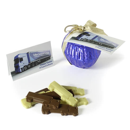 A purple foil-wrapped Easter egg with a gold ribbon, featuring a business card with a truck design and brown and white chocolate truck-shaped pieces. Product: Corporate Easter Egg with Customisable Filling.