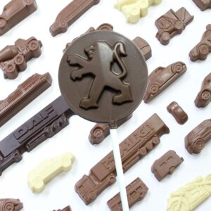 A Peugeot Chocolate Gifts set features a round lollipop with a lion emblem alongside chocolate shapes of vehicles like cars, trucks, and construction equipment.