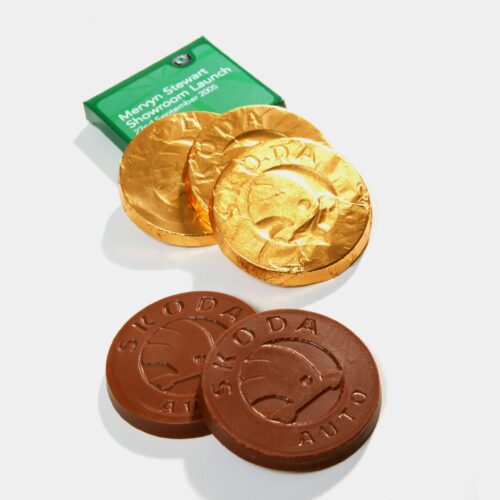 Skoda Chocolate Gifts are displayed: some coins with Skoda logos are wrapped in gold foil, others unwrapped. A green card in the background notes a showroom launch in May 2005.