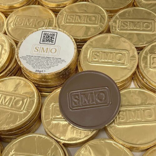 smo_coin_with_label_-_lighter_colour A stack of Bespoke Chocolate Coins wrapped in gold foil, one unwrapped to show the chocolate inside, featuring the label "SMO.