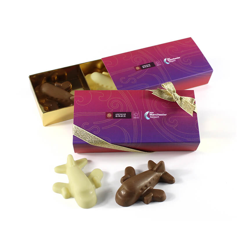 Box of airplane-shaped chocolates, open to reveal a mix of white and milk chocolates inside, with a gold decorative ribbon on the box.