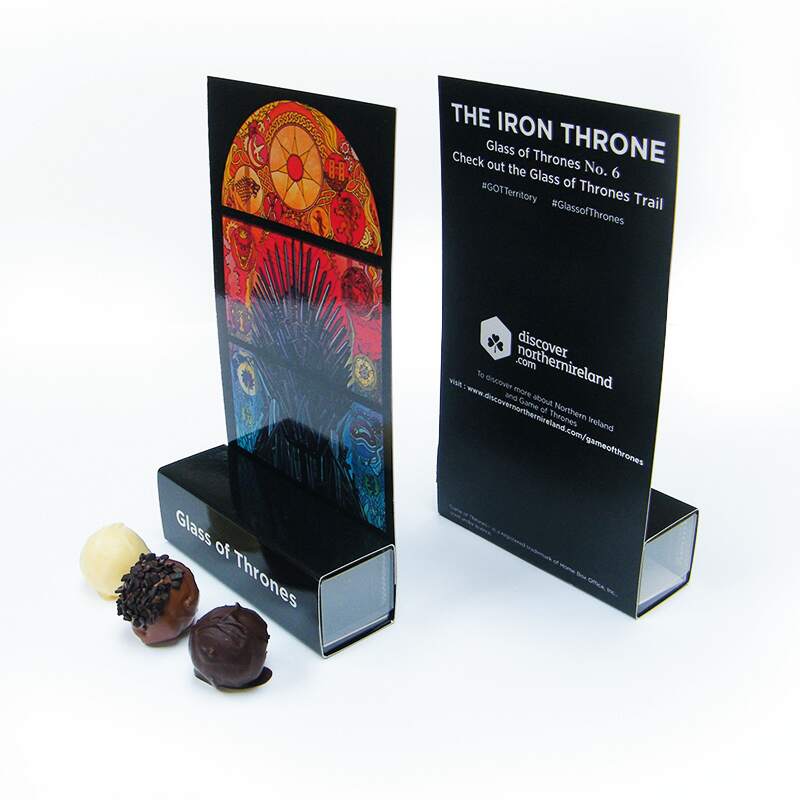Two cards labelled Glass of Thrones stand upright in holders, with images and text about the Iron Throne. Three assorted chocolates are placed in front of the holders.