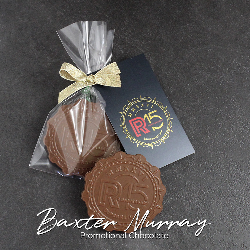 Bespoke circular chocolate with a logo at the centre, in a clear cellophane gift bag closed with a hand tied gold ribbon attaching an oversized branded gift tag with a gold print.