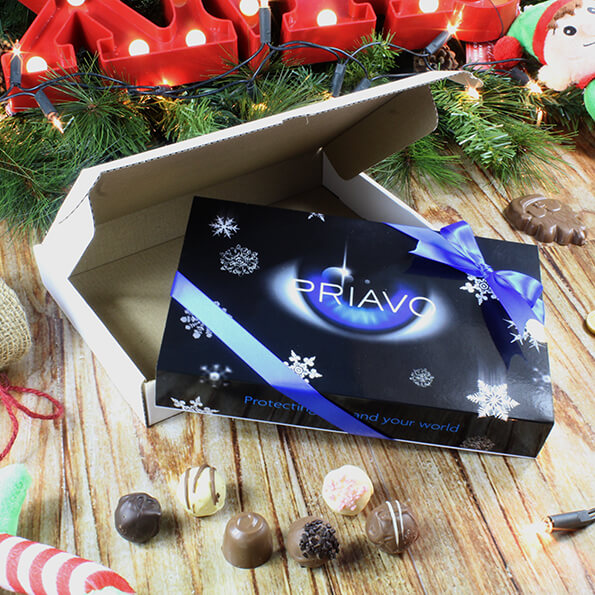 An open postal outer under a Christmas tree with a luxury chocolate box with a brnded black lid and blue hand tied ribbon.