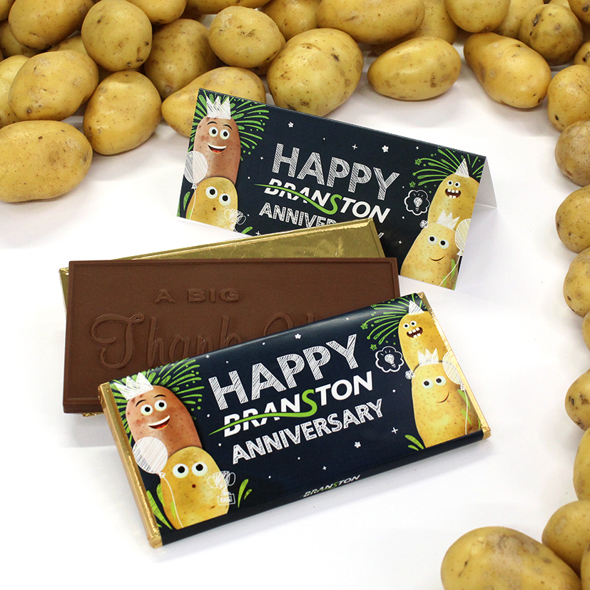 How to design a campaign around branded chocolate with a milk chocolate bar with the message-"A Big Thank You" embossed in the chocolate inside a wrapper with Happy Branston Anniversary design printed on it. The chocolate bars are surrounded by potatoes.